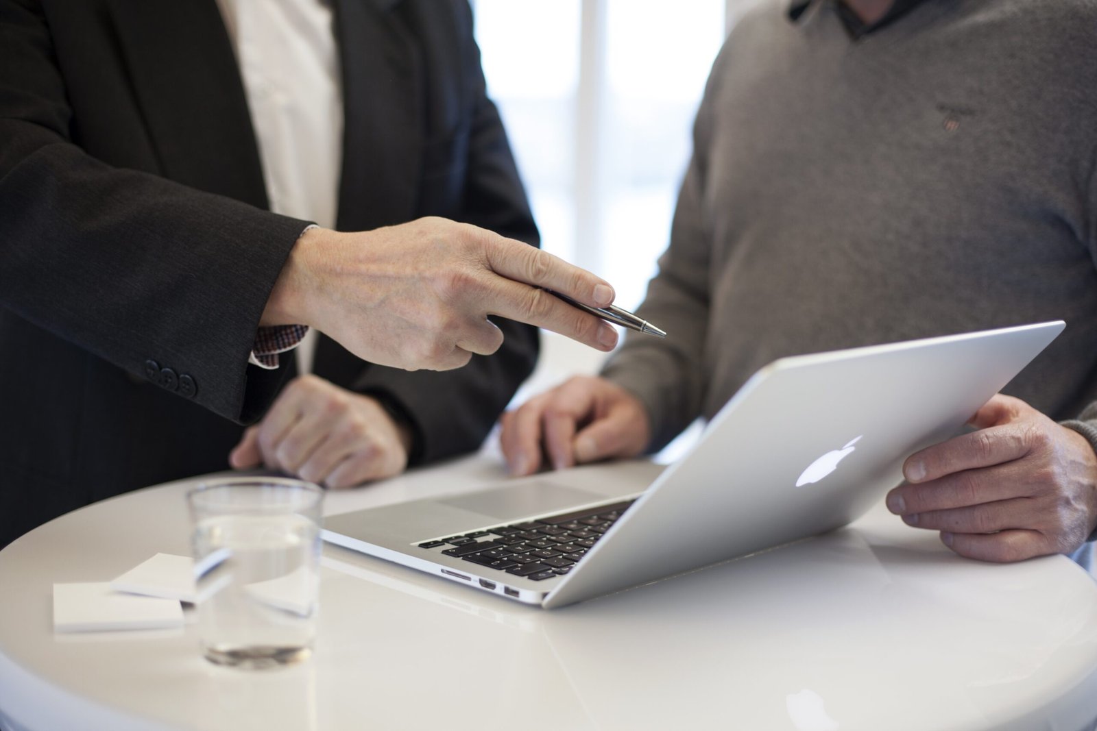 Two professionals discuss a laptop screen at a white table, one pointing with a pen